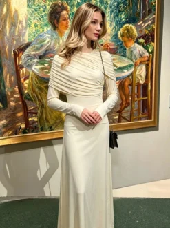 Robe de soirée élégante et moulante couleur crème épaules drapées et manches longues.
