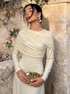 Robe de soirée élégante et moulante couleur crème épaules drapées et manches longues.