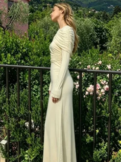 Robe de soirée élégante et moulante couleur crème épaules drapées et manches longues.